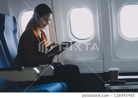 Asian woman working and planning on an airplane. Asian woman reading a book while sitting on an airplane. Asian woman working and planning on an airplane. Asian woman reading a book while sitting on an airplane. 116843493