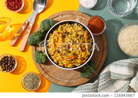 Pilaf in bowl, board, towel and spices on yellow and green background, top view Pilaf in bowl, board, towel and spices on yellow and green background, top view 116843667