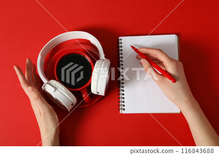 A cup of coffee with headphones and a notebook on a red background 116843688