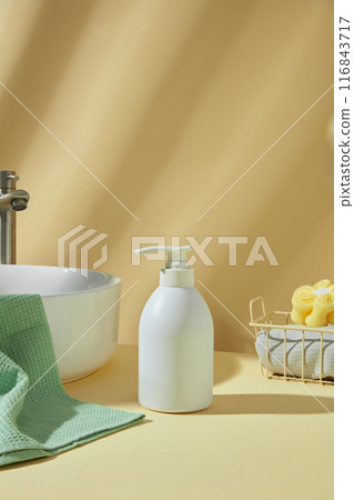 A white blank label cosmetic bottle for personal hygiene placed on yellow countertop, featured on yellow background. Sink, towel and bath sponge decorated around, empty space for adding text 116843717