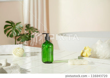 Frontal shot at a unbranded green shampoo bottle, which displayed on a brick bathroom floor, surrounded by some items for bathing. Blank space for advertising or adding text 116843720