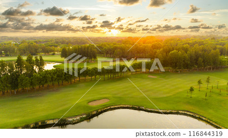 Golf course at sunset with beautiful sky and sand trap. Scenic panoramic view of golf fairway with bunker. Golf field with pines 116844319