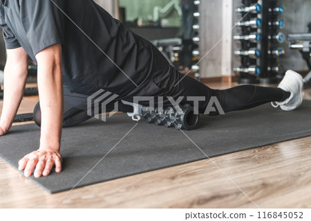 一名男子在健身房使用泡沫軸來放鬆大腿的肌筋膜。 116845052