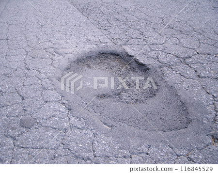 An asphalt road with holes appearing again in areas that had previously been repaired 116845529