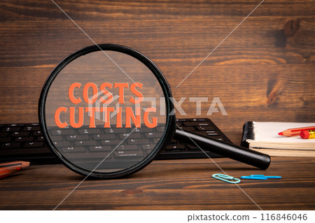 Costs cutting Concept. Magnifying glass and computer keyboard on wooden table 116846046