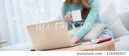 Young asian woman wearing glasses sitting sofa working on laptop computer and drinking coffee. 116846807