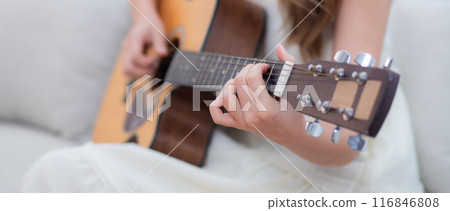 Closeup hands of young asian woman sitting on sofa playing guitar in living room. 116846808