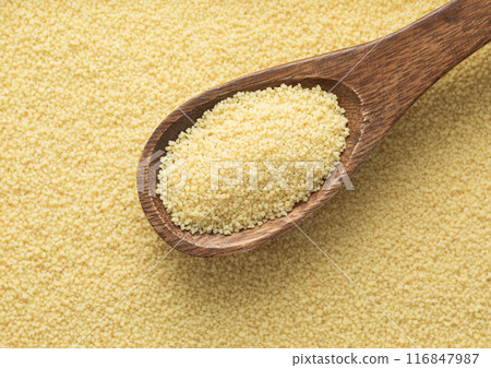 Yellow raw organic healthy couscous grain seeds on wooden spoon textured background. 116847987