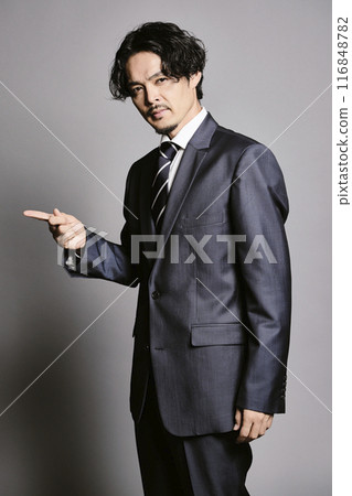 A man in a suit standing against a grey background 116848782