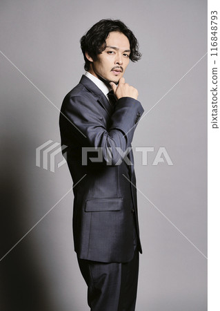 一個穿著西裝的男人站在灰色的背景下 116848793