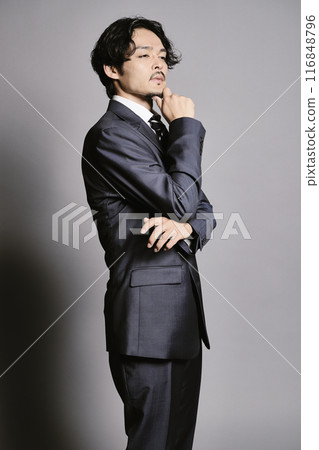 A man in a suit standing against a grey background A man in a suit standing against a grey background 116848796