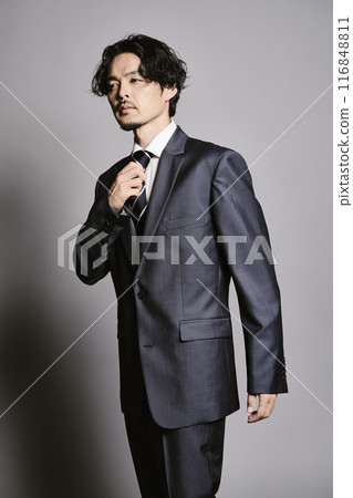 一個穿著西裝的男人站在灰色的背景下 116848811