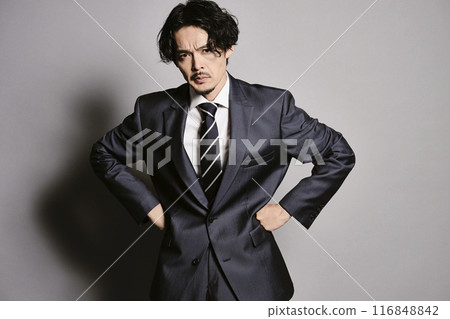 A man in a suit standing against a grey background 116848842