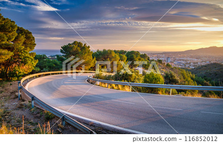 winding road that curves gently to the left as it meanders through a scenic landscape. The road is bordered by guardrails for safety and is surrounded by lush greenery winding road that curves gently to the left as it meanders through a scenic landscape. The road is bordered by guardrails for safety and is surrounded by lush greenery 116852012