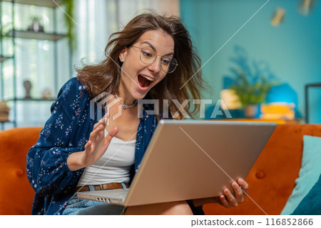 Surprised happy young woman in eyeglasses using laptop computer, receive good news message at home Surprised happy young woman in eyeglasses using laptop computer, receive good news message at home 116852866