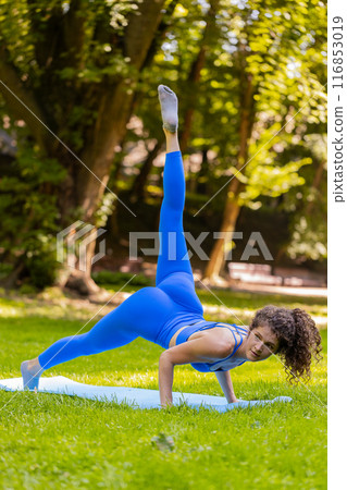 Caucasian young woman in yoga Cobra pose stretches upward morning fitness routine on mat in park 116853019