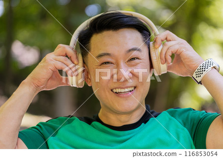 Happy young Japanese runner jogger man put on wireless modern headphones earphones listening music 116853054
