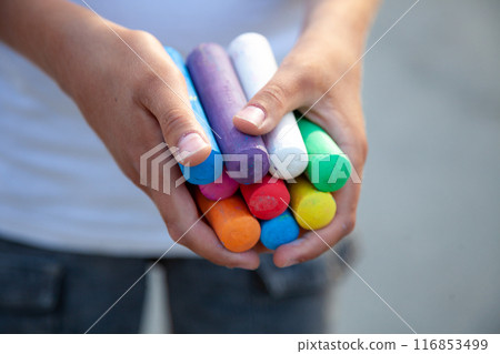 Chalks. Large multi-colored crayons in children's hands. The child holds the chalk. Draw on the street. Fascinating drawing for children Chalks. Large multi-colored crayons in children's hands. The child holds the chalk. Draw on the street. Fascinating drawing for children 116853499
