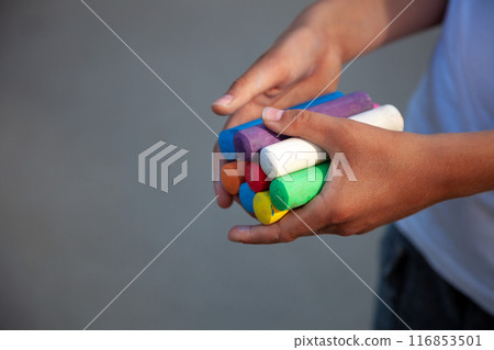 Chalks. Large multi-colored crayons in children's hands. The child holds the chalk. Draw on the street. Fascinating drawing for children Chalks. Large multi-colored crayons in children's hands. The child holds the chalk. Draw on the street. Fascinating drawing for children 116853501