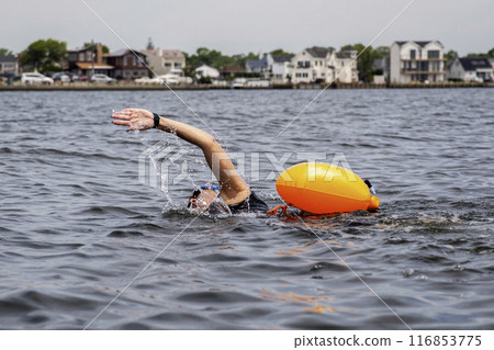 Female swimmer swimming in the open water wearing an orange floatation for safety 116853775
