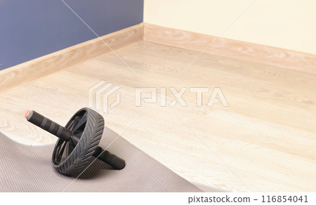 Fitness gymnastic wheel with two handles on mat in room. Equipment for sports activities. Health and movement.  116854041