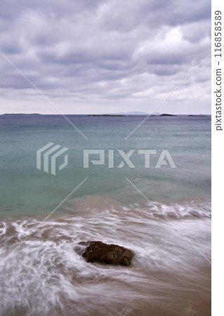 long exposure beach waves around rock cloudy day 116858589