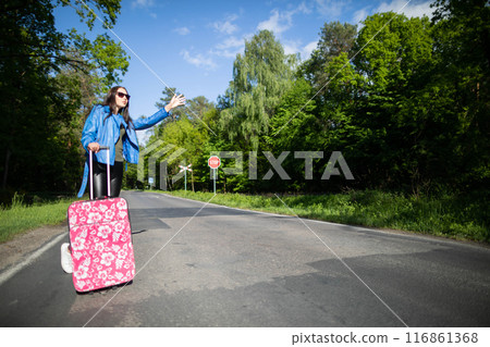 A teenager is standing with a pink suitcase on wheels and tries to stop the opportunity to go on vacation faster. A teenager is standing with a pink suitcase on wheels and tries to stop the opportunity to go on vacation faster. 116861368