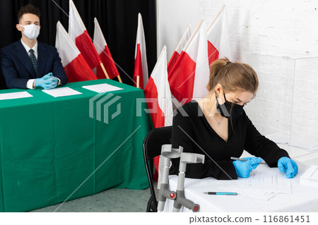 A teenager with orthopedic crutches sits at the polling station and fills out ballots for the president of Poland. 116861451