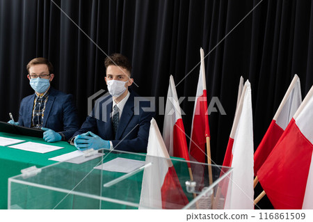 An election commission consisting of two young adult men sits and waits for voters. An election commission consisting of two young adult men sits and waits for voters. 116861509