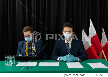 An election commission consisting of two young adult men sits and waits for voters. An election commission consisting of two young adult men sits and waits for voters. 116861510