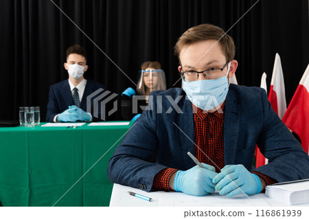The young voter fills out the ballot paper with his hand covering the place where he is writing. The young voter fills out the ballot paper with his hand covering the place where he is writing. 116861939