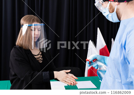 A woman from an election commission disinfects her hands before sitting at an election table. A woman from an election commission disinfects her hands before sitting at an election table. 116862009