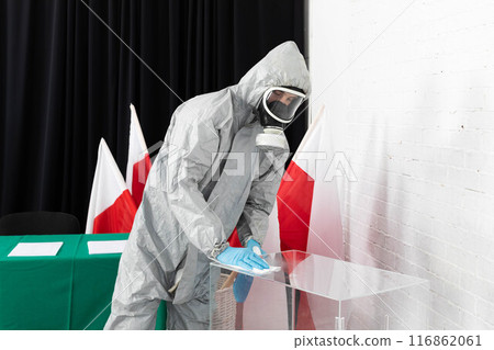 An employee in a special overalls and a filter mask thoroughly disinfects the polling station. Presidential election in Poland. 116862061