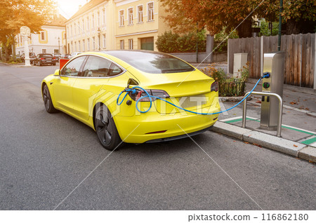 Vienna, Austria, August 22, 2022. In the village of Grinzing an electric car was parked and connected to the charging station. Modern transport technology and low environmental impact. Copy space Vienna, Austria, August 22, 2022. In the village of Grinzing an electric car was parked and connected to the charging station. Modern transport technology and low environmental impact. Copy space 116862180