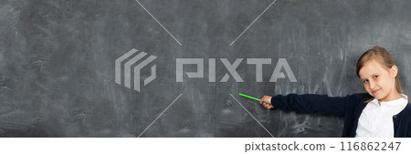 Schoolgirl shows on an empty school board. He is standing in the classroom at the chalkboard. Younger girl. Panoramic image. 116862247