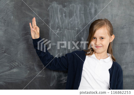 Schoolgirl shows on an empty school board. He is standing in the classroom at the chalkboard. Younger girl. 116862253