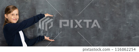 Schoolgirl shows on an empty school board. He is standing in the classroom at the chalkboard. Younger girl. Panoramic image. 116862254