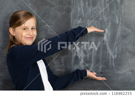 Schoolgirl shows on an empty school board. He is standing in the classroom at the chalkboard. Younger girl. 116862255
