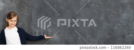 Schoolgirl shows on an empty school board. He is standing in the classroom at the chalkboard. Younger girl. Panoramic image. Schoolgirl shows on an empty school board. He is standing in the classroom at the chalkboard. Younger girl. Panoramic image. 116862260