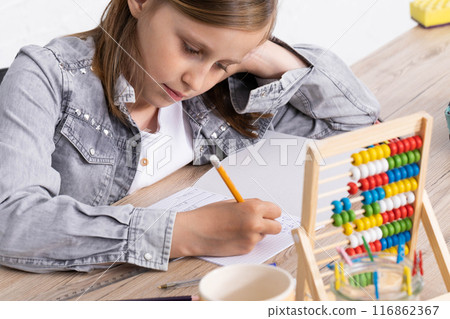 The girl solves the task given in the classroom. The schoolgirl diligently writes in a notebook. 116862367