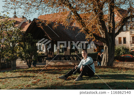 Professional Photographer Taking Picture Of Beautiful Autumn Park. Man Professional Photographer Sit With Camera And With Smartphone In Autumn Park. Retouched, Vibrant Colors, Brownish Tones. 116862540