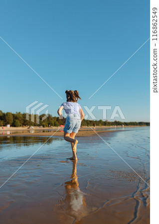 Girl of 6 years back view in in shorts and T-shirt running back view on beach in summer Girl of 6 years back view in in shorts and T-shirt running back view on beach in summer 116862549