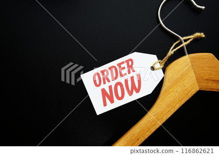 Order Now on price tag with wooden clothes hanger top view on black background Order Now on price tag with wooden clothes hanger top view on black background 116862621