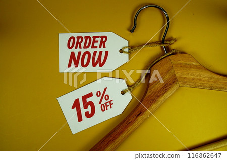 Order Now and Sale 15% on price tag with wooden clothes hanger top view on yellow background Order Now and Sale 15% on price tag with wooden clothes hanger top view on yellow background 116862647