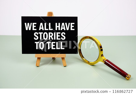 We all have stories to tell text on paper card with magnifying glass on green background 116862727