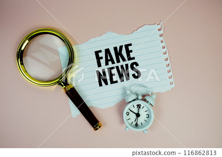 Fake News text on paper torn with alarm clock and magnifying glass top view on purple background 116862813