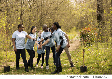 Cheerful enthusiastic team of activists unite to plant trees in the woods, taking action to protect natural environment. People celebrating their voluntary work by connecting hands together. Cheerful enthusiastic team of activists unite to plant trees in the woods, taking action to protect natural environment. People celebrating their voluntary work by connecting hands together. 116863879