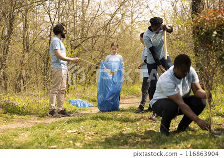 People collaborating to use proper tools and clean the forest, recycling plastic waste and fighting pollution. Activists team volunteering to collect rubbish from the woodland ecosystem. 116863904