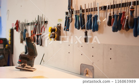 Close up of electric router on workbench in assembly shop with woodworking tools on rack in background. Focus on hand powered gear used for cutting wood in carpentry studio, panning shot Close up of electric router on workbench in assembly shop with woodworking tools on rack in background. Focus on hand powered gear used for cutting wood in carpentry studio, panning shot 116863989