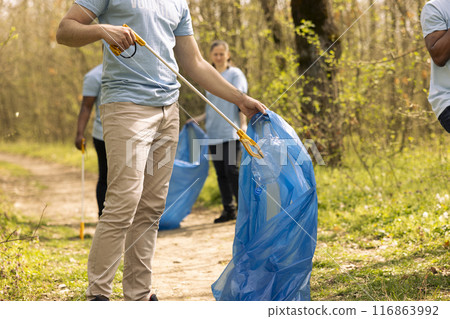 Male volunteer collecting rubbish to fix pollution issues within the habitat, protecting the natural ecosystem. Activist doing voluntary work to clean the woods from trash and plastic waste. Male volunteer collecting rubbish to fix pollution issues within the habitat, protecting the natural ecosystem. Activist doing voluntary work to clean the woods from trash and plastic waste. 116863992